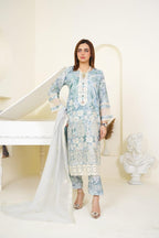 Woman in a light blue floral dress with white dupatta standing in a minimalistic room.