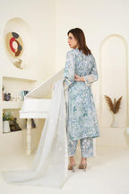 Woman in a light blue floral outfit standing in a bright room with white walls and a piano.