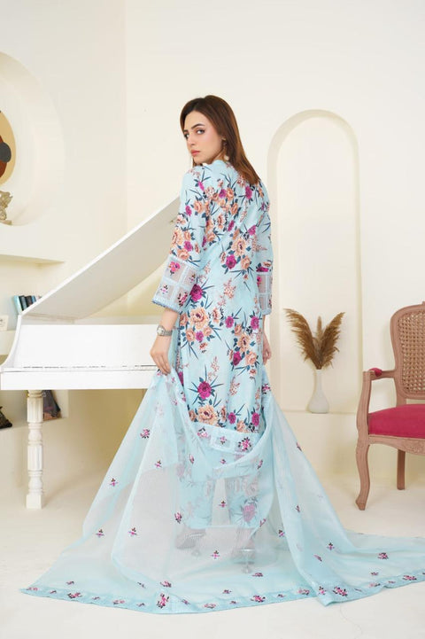 Woman wearing a floral dress with a light blue dupatta in a decorated room.