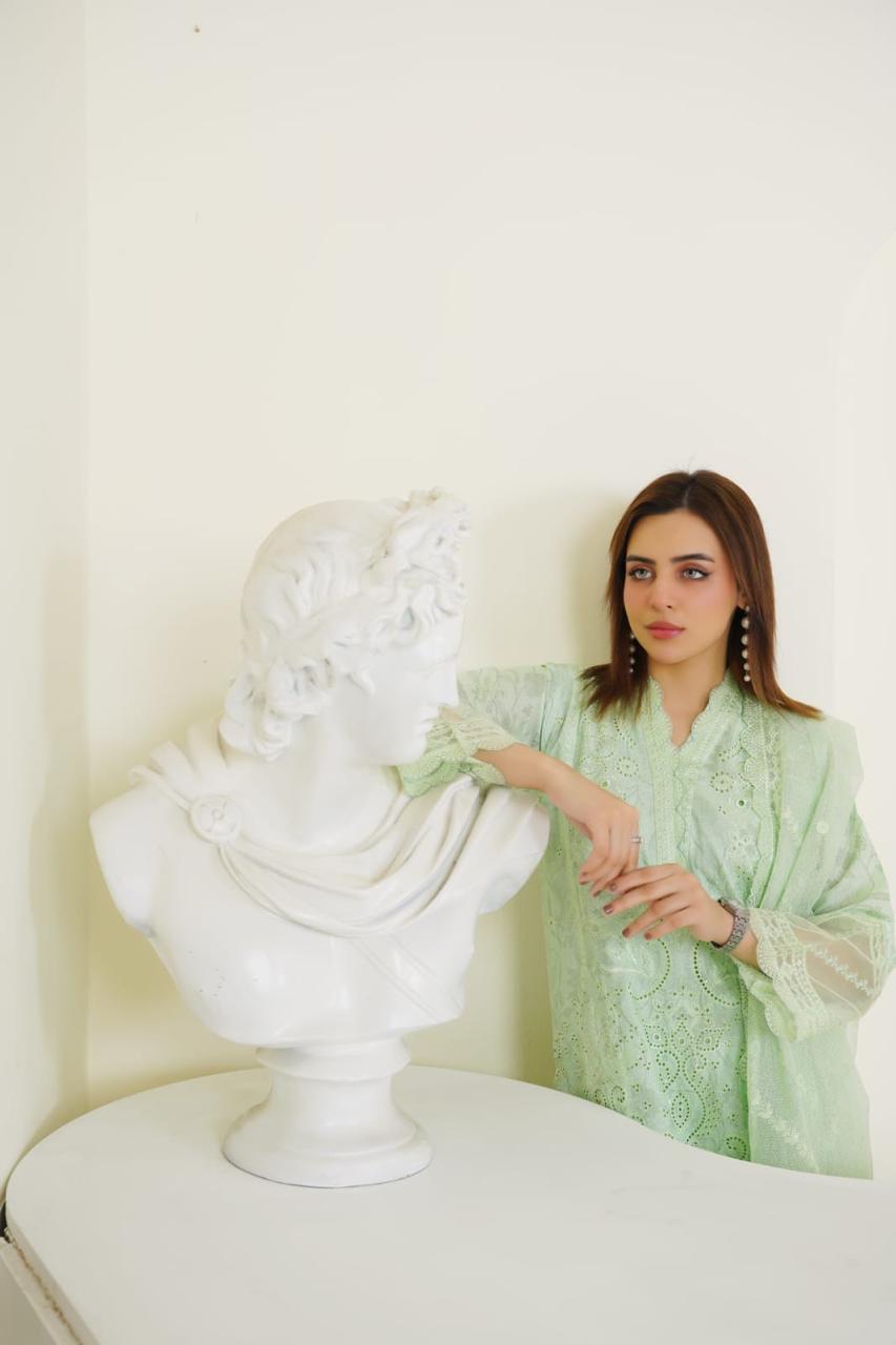 Woman in a light green dress standing next to a white bust sculpture indoors.